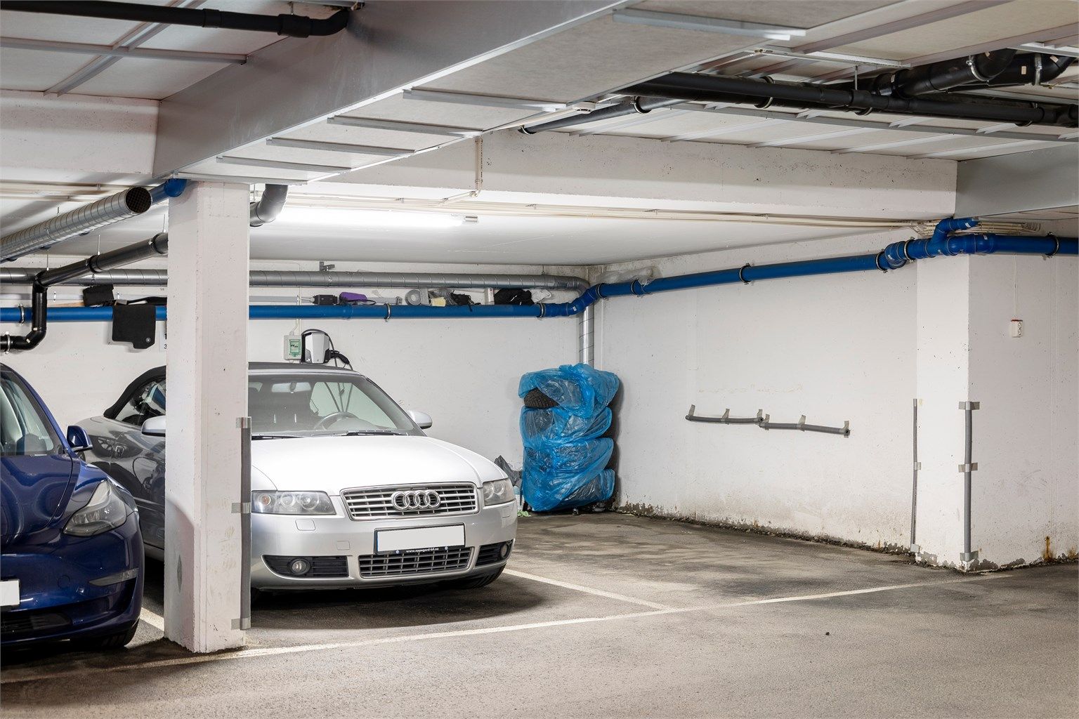 Med boligen følger fast parkeringsplass (til høyre i bilde) og en bod på 5 m² i felles, underjordisk garasjeanlegg. Mulighet for kjøp av garasjeplass (til venstre i bilde)