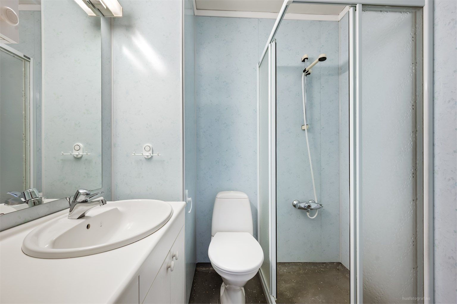 Badet har terrazzo på gulv, baderomsplater på veggene og er utstyrt med dusjhjørne, toalett og servant.