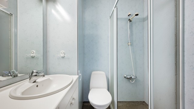Badet har terrazzo på gulv, baderomsplater på veggene og er utstyrt med dusjhjørne, toalett og servant.