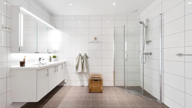 Flislagt bad med gulvvarme. Romsling baderomsinnredning med hvite glatte fronter og ovenpåliggende servant. Speilskap med lys over servant.