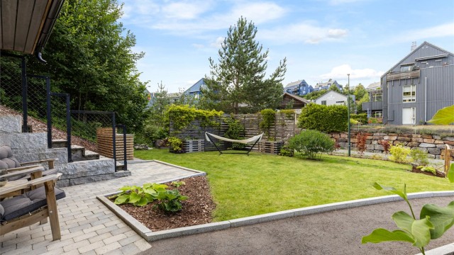 Boligens inngangsparti er pent opparbeidet med plen, belegningsstein og diverse beplantninger. På siden av bygningen er det en trapp som leder opp til takterrassen.