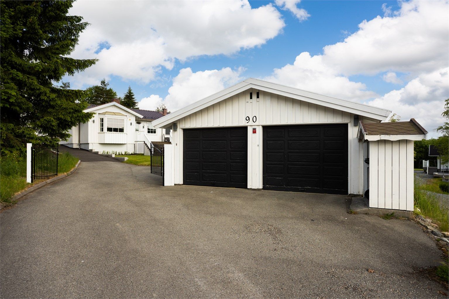 Asfaltert gårdsplass med dobbelgarasje og smijernsport videre inn til hagen.
