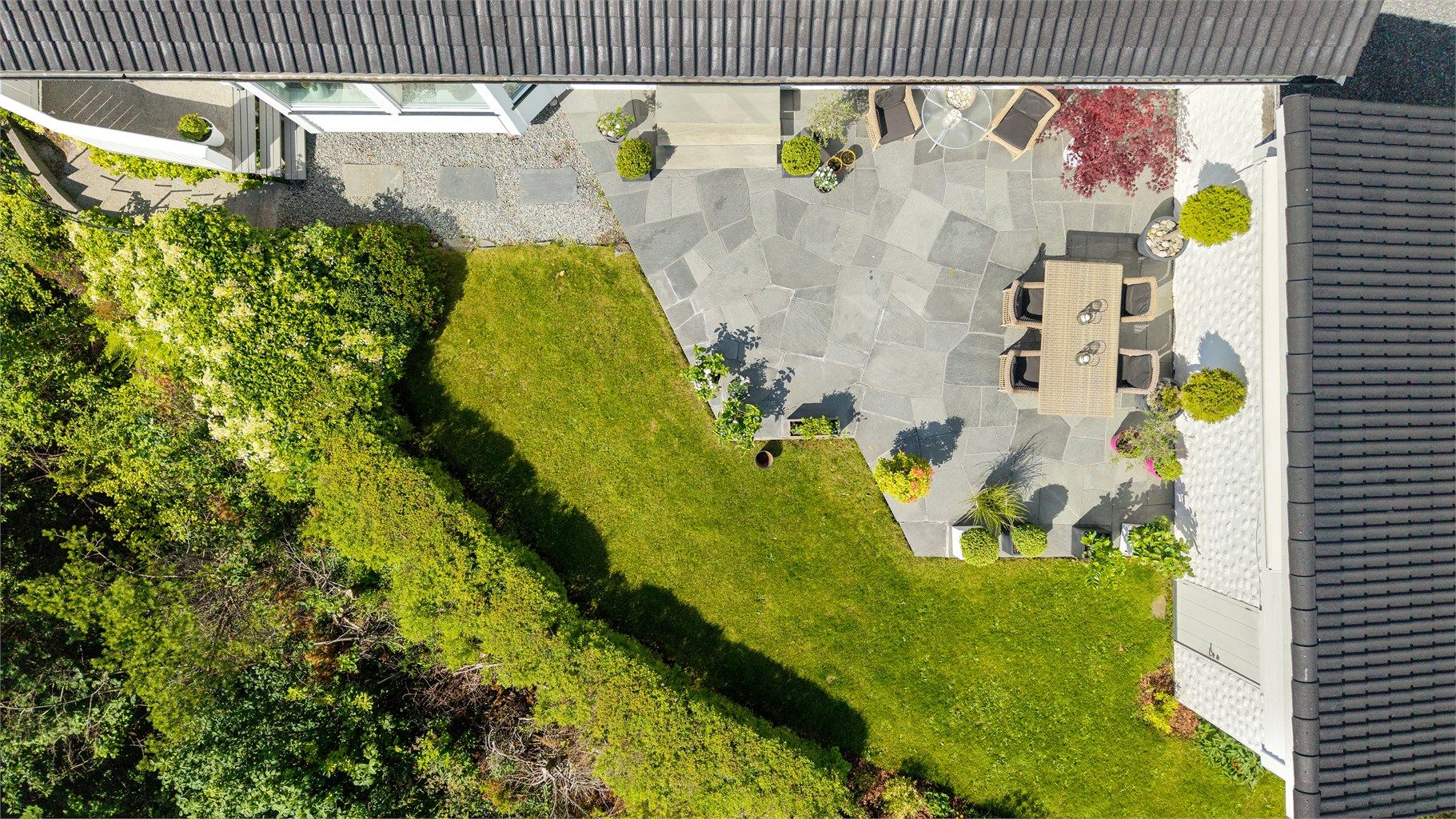 Tomten er opparbeidet med plen, beplantning og skiferterrasse.
