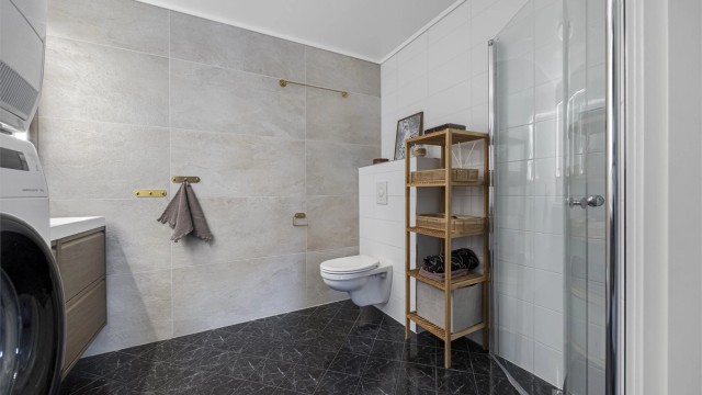 Rommet er praktisk innredet med dusjhjørne, vegghengt toalett og opplegg for vaskemaskin.