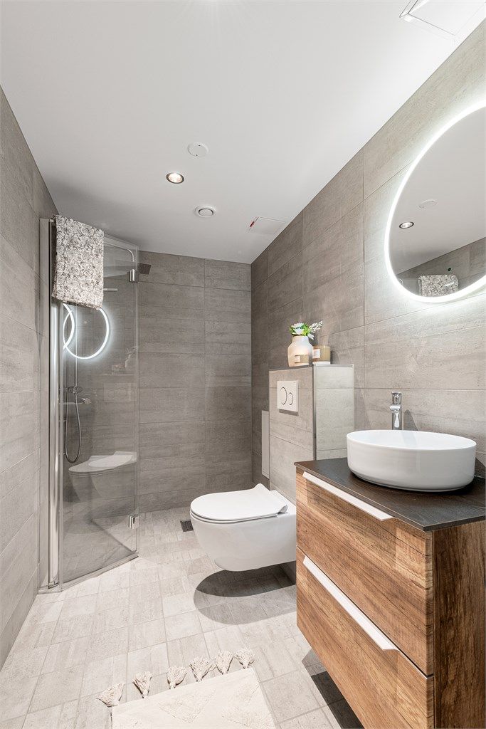 Stilren innredning med ovenpåliggende servant og et stort, rundt speil med integrert belysning