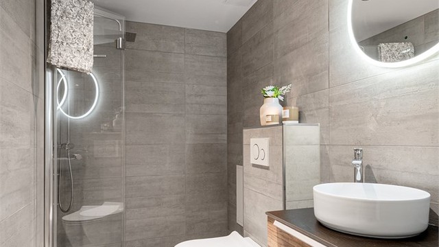 Stilren innredning med ovenpåliggende servant og et stort, rundt speil med integrert belysning