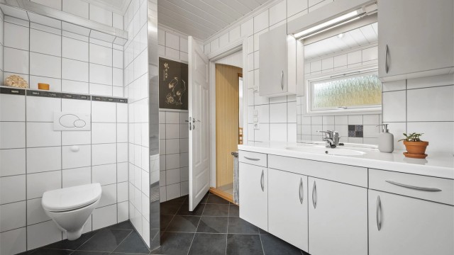 Badet er utstyrt med vegghengt toalett og innfliset badekar med dusjvegg av glass samt veggmontert dusjarmatur