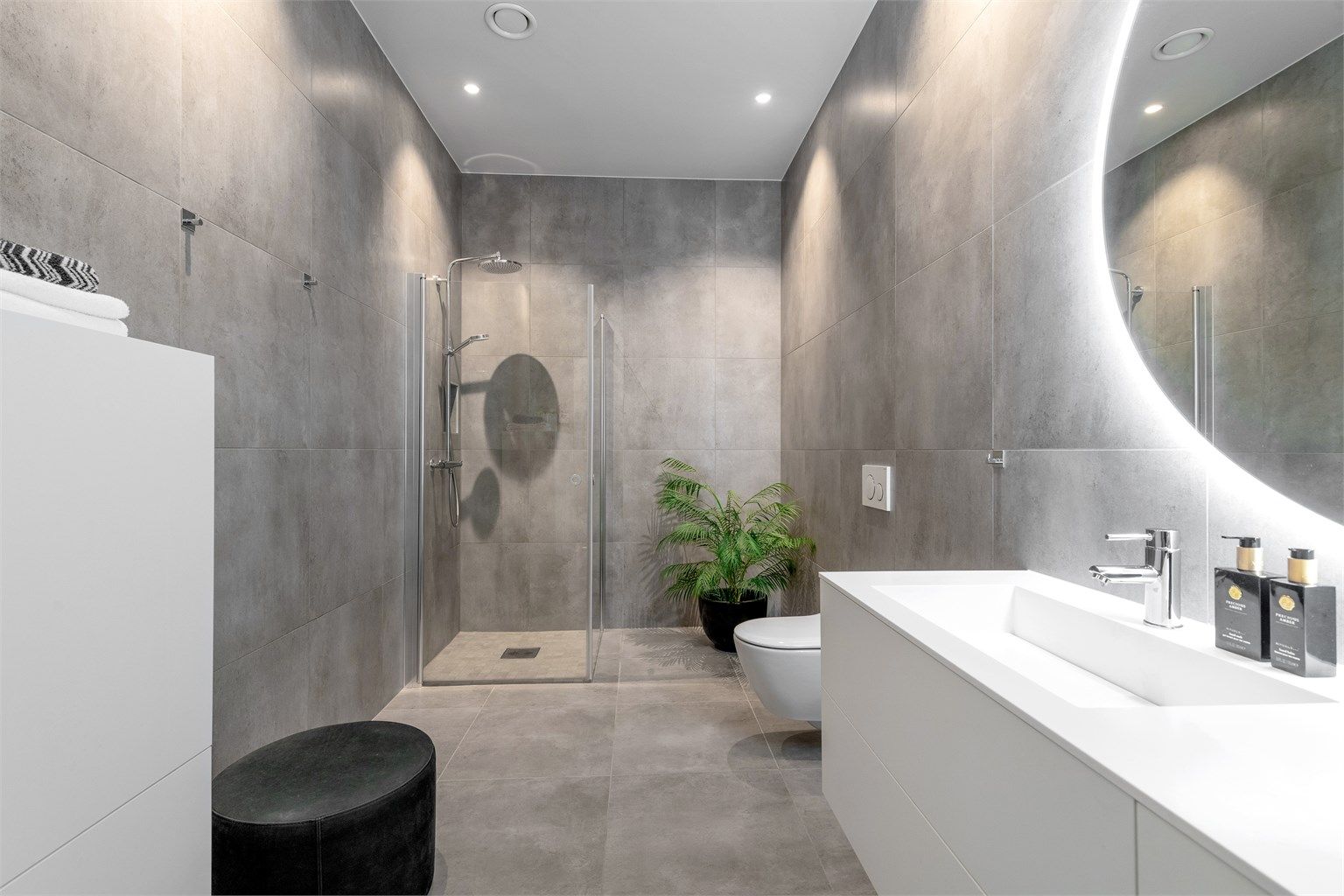 Badet har dusjhjørne med glassvegger og vegghengt dusjarmatur med hånddusj og regndusj. Vegghengt toalett.