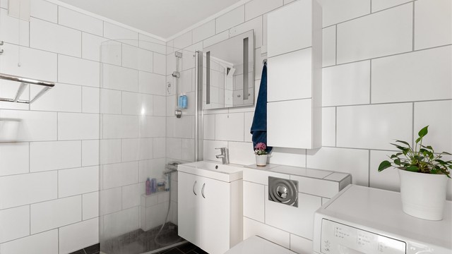 Pent og flislagt baderom med gulvvarme, dusj med foldbare dører og opplegg for vaskemaskin og tørketrommel