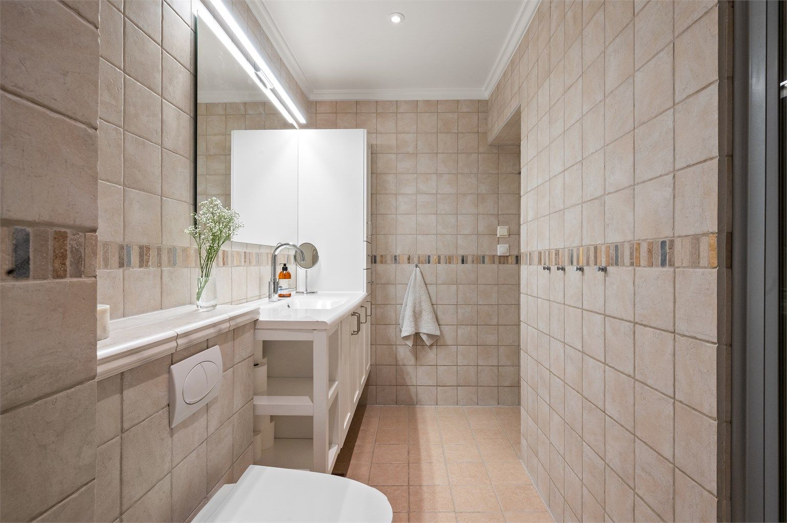 Badet er innredet med vegghengt toalett, servant med underskap og innfelte LED-downlights i taket.