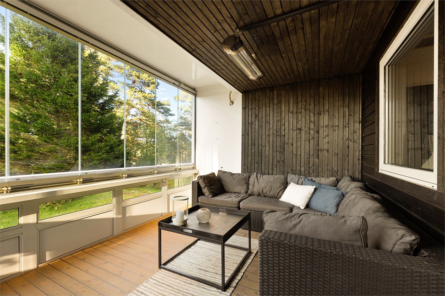 Innglasset veranda med skjermet skogutsikt, lune trepanel og lys som gir en lun og rolig utefølelse.