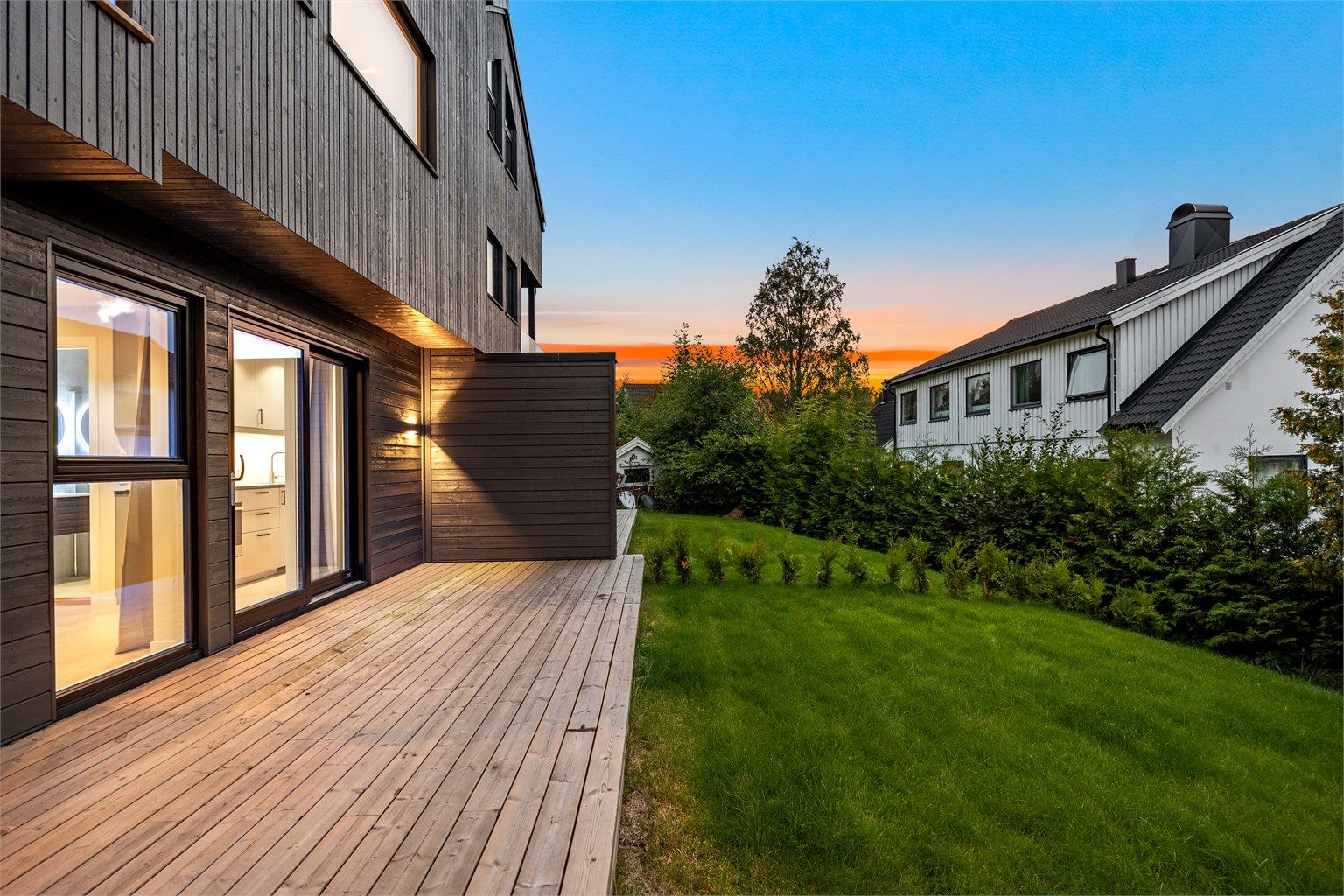 Markterrasse i første etasje med utgang til skjermet gressplen omkranset av hekk.