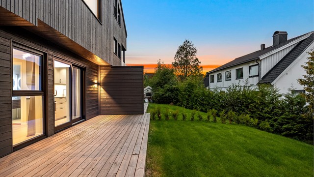 Markterrasse i første etasje med utgang til skjermet gressplen omkranset av hekk.