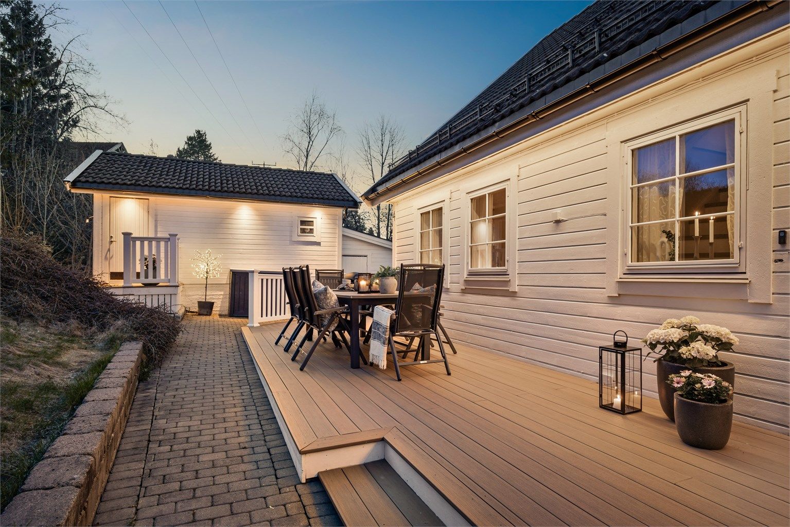 Asfaltert adkomst til garasjen fra 2024 og belegningsstein langs deler av husveggen.