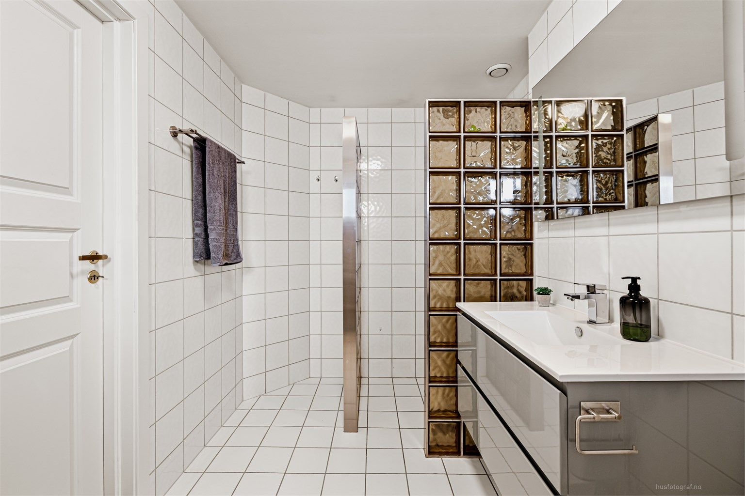 Badet har en romslig dusjnisje med glassvegg, vegghengt servantinnredning og gulvstående toalett.