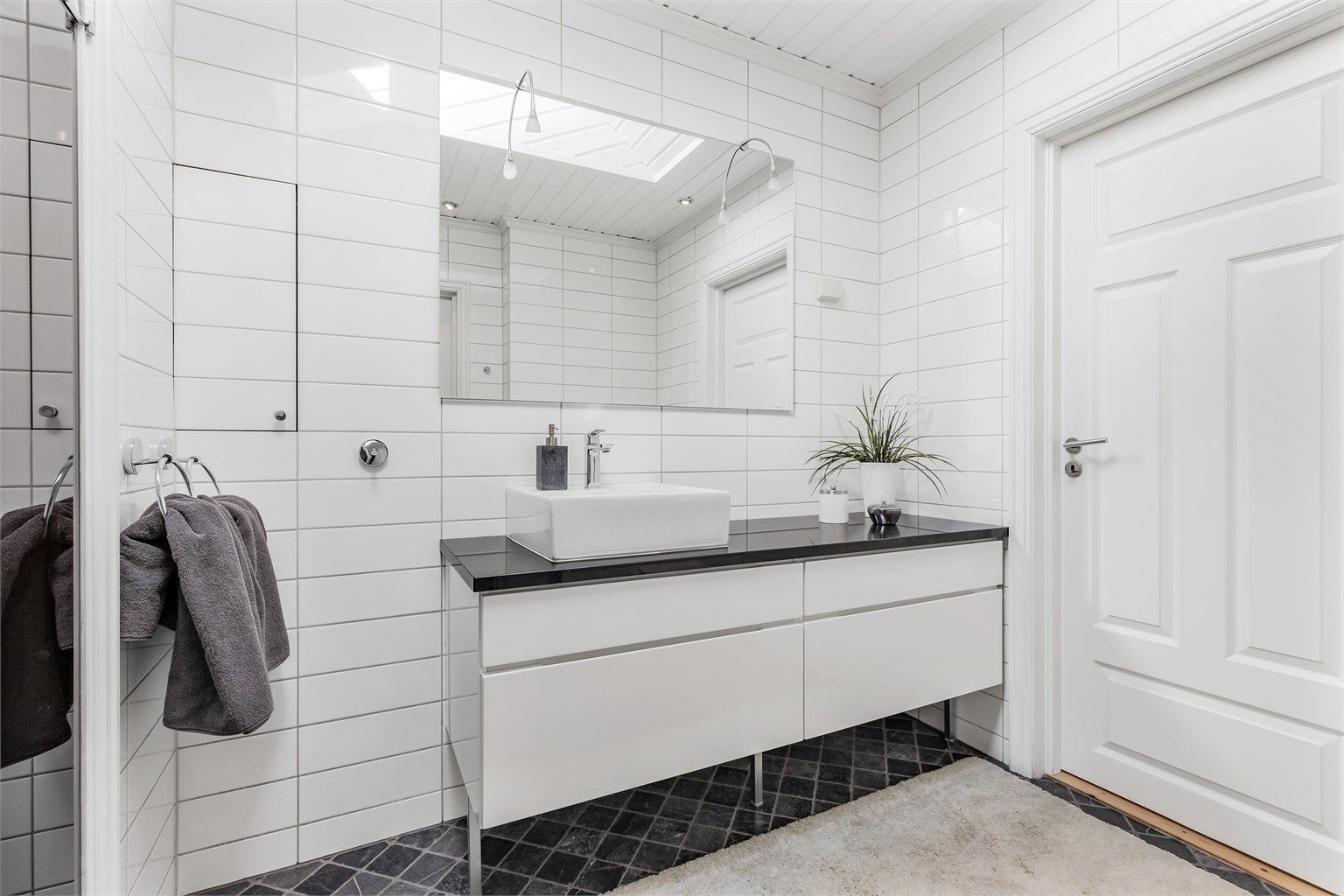 Baderom fra byggeår. Flislagt gulv med gulvvarme. Flislagte vegger. Trekledning og fliser i himling. Vegghengt servantinnredning. Speil med overlys.