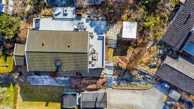 Tomten er eiet og angitt til 857 kvm., her sett i fugleperspektiv med vest mot nedre bildekant. I garasjen og oppkjørselen er det oppstillingsmulighet for tre-fire biler.