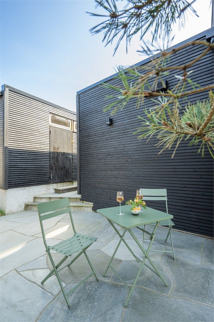 En liten, skjermet uteplass ved inngangspartiet, belagt med naturskifer.