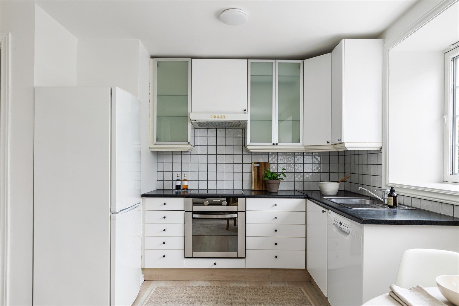 Praktisk kjøkken med flislagt bakvegg over benk og opplegg for oppvaskmaskin.