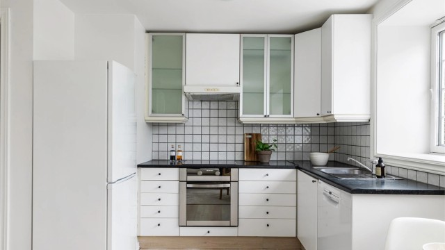 Praktisk kjøkken med flislagt bakvegg over benk og opplegg for oppvaskmaskin.