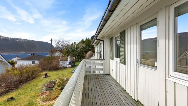 Verandaen strekker seg langs deler av fasaden mot sør og er bygget med et rekkverk i treverk.