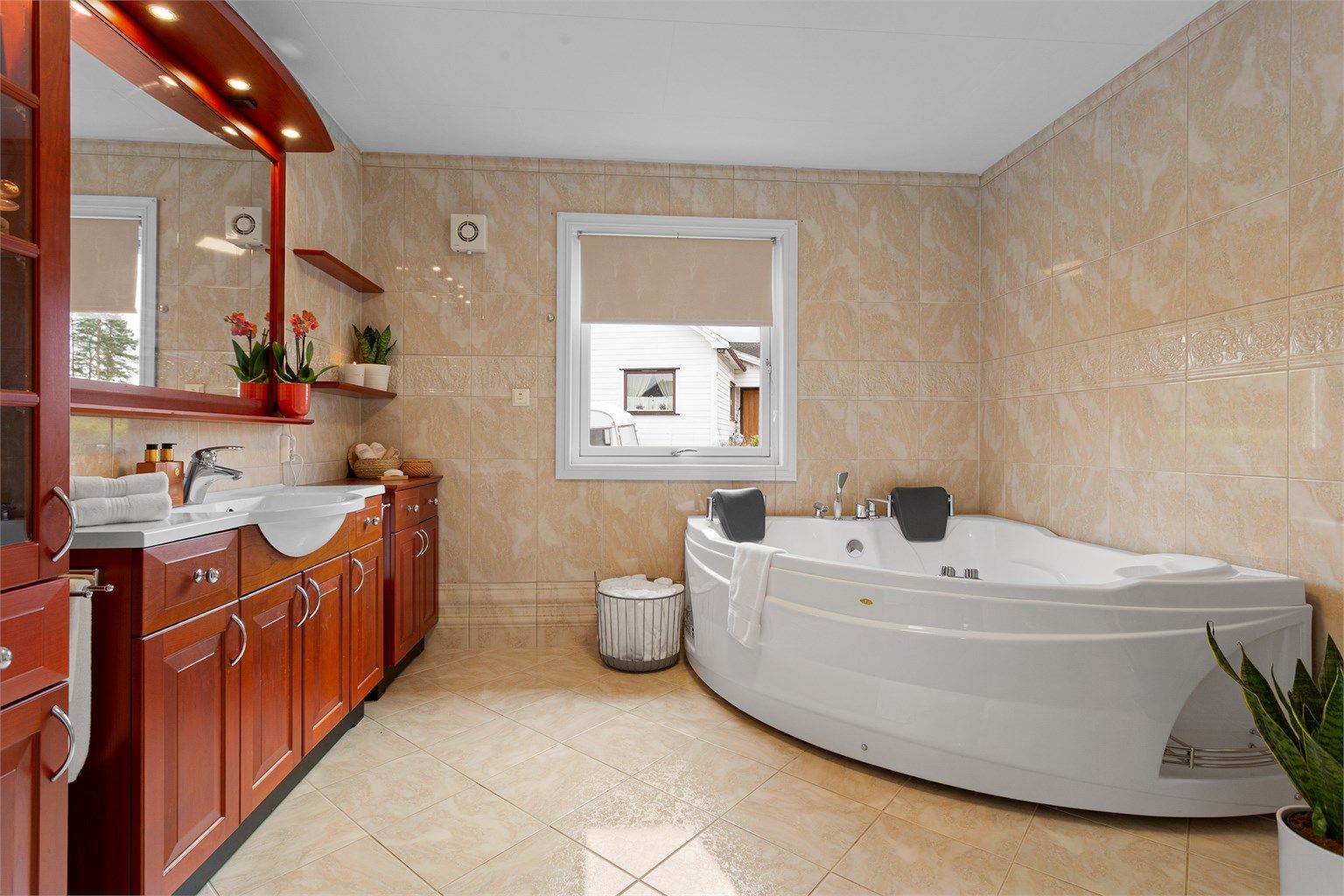 Hjørnebadekar med hånddusj, tappekran og dyser. Gulvstående toalett og avtrekksvifte plassert på yttervegg