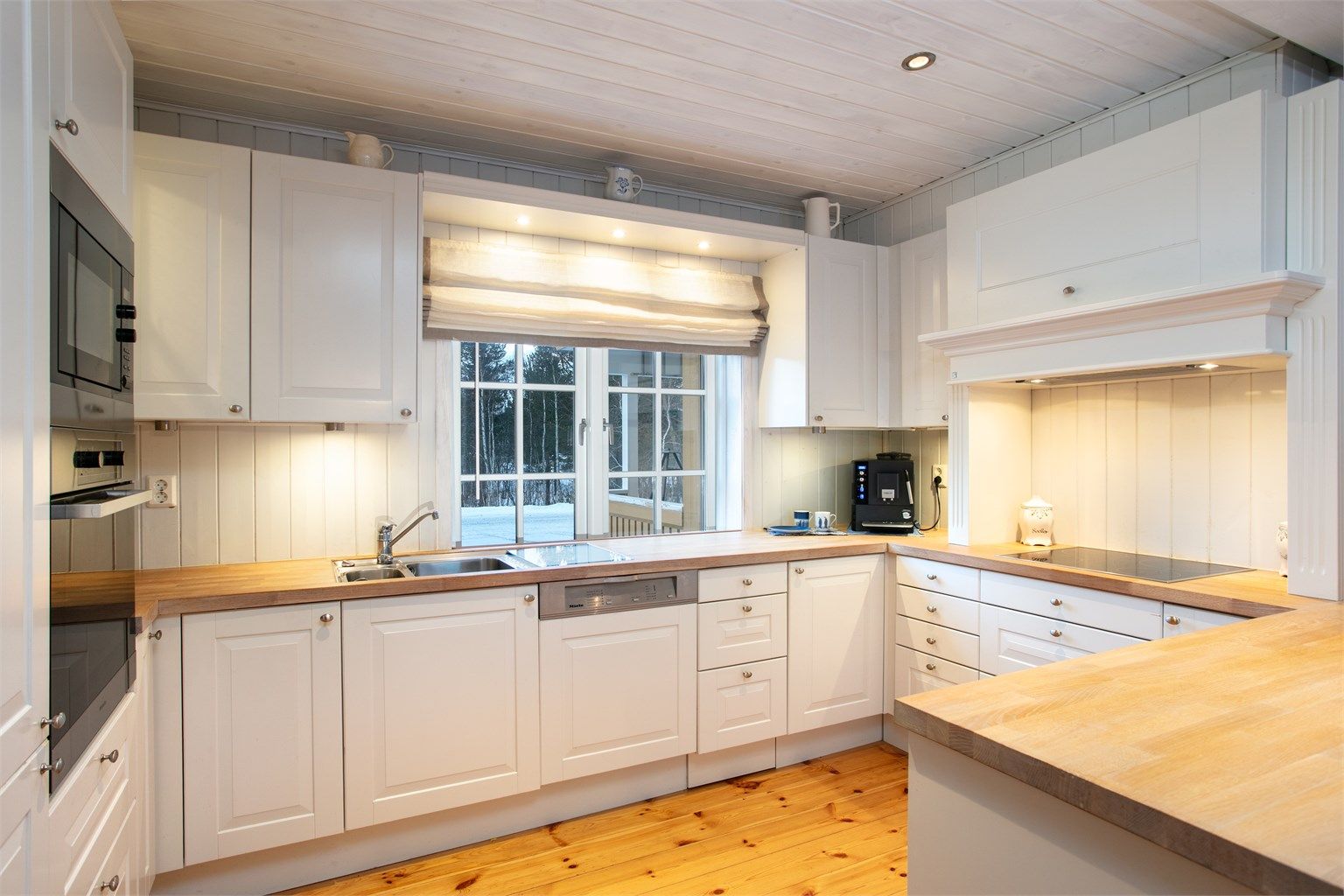 Hvit profilert kjøkkeninnrending med integrete hvitevarer og heltre benkeplate