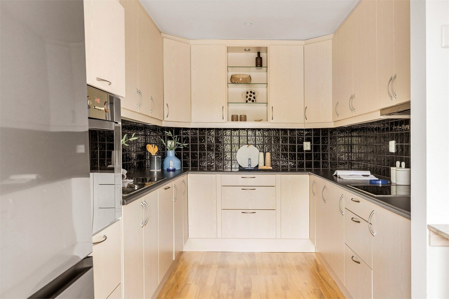 Kjøkkenet har innredning med glatte fronter og benkeplate i laminat. Mellom benkeplate og overskap er det fliser.