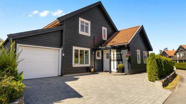 Pent inngangsparti med belegningsstein og beplantning. Garasje med el-bil lader samt parkering til 2 biler utenfor.