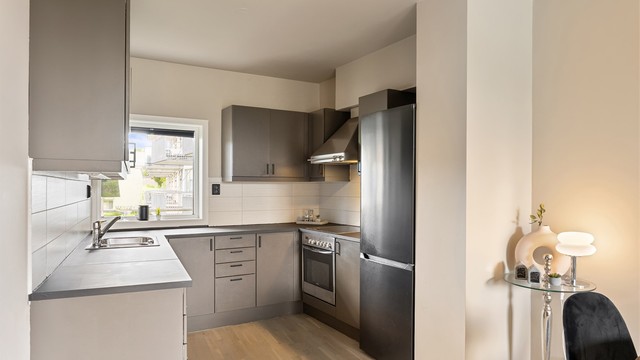 Kjøkkenet ligger naturlig tilbaketrukket fra stuen og er innredet med slette flater og malt heltre benkeplate.