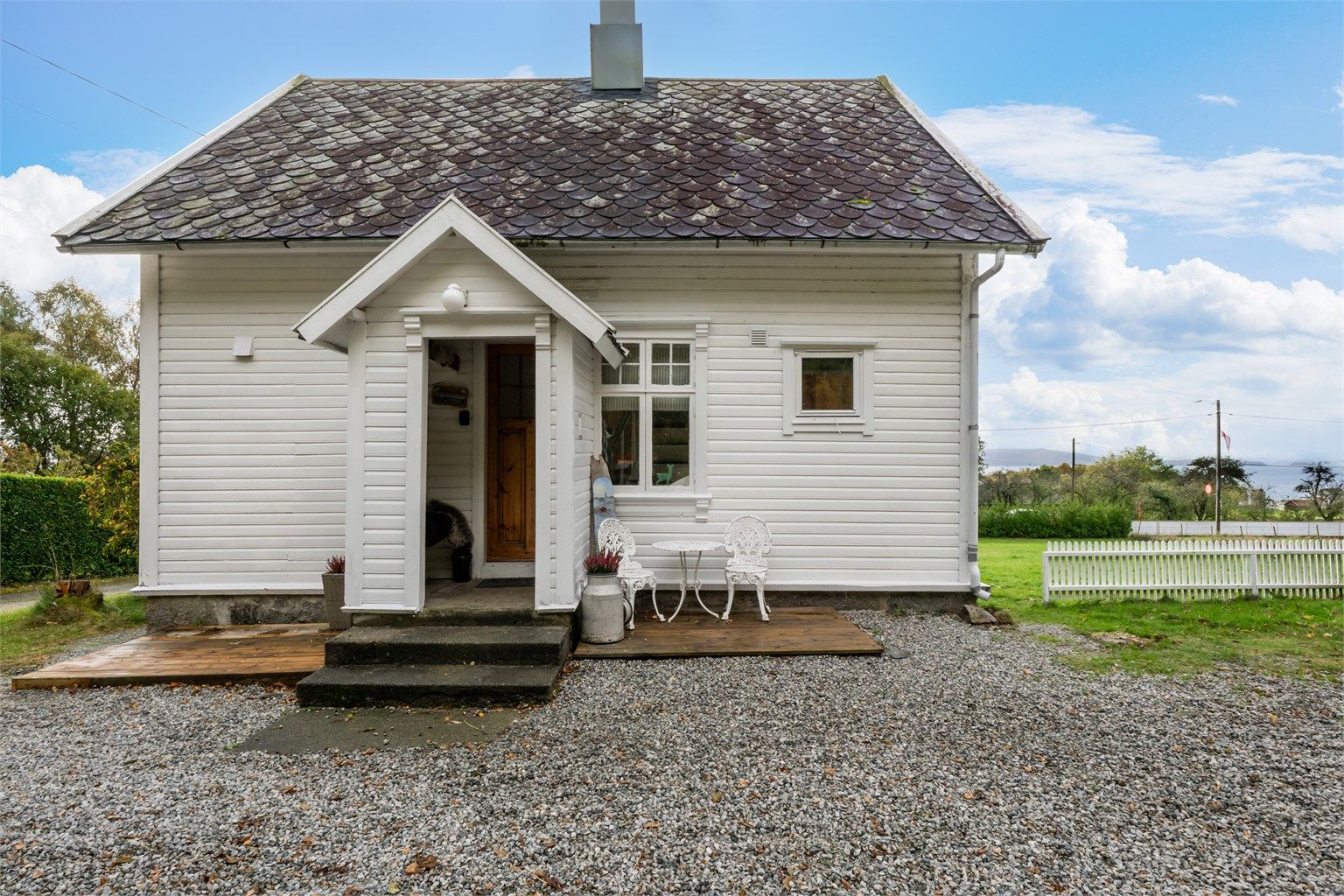 Overbygd inngangsparti med terrasseplatting og gruset adkomst foran boligen.