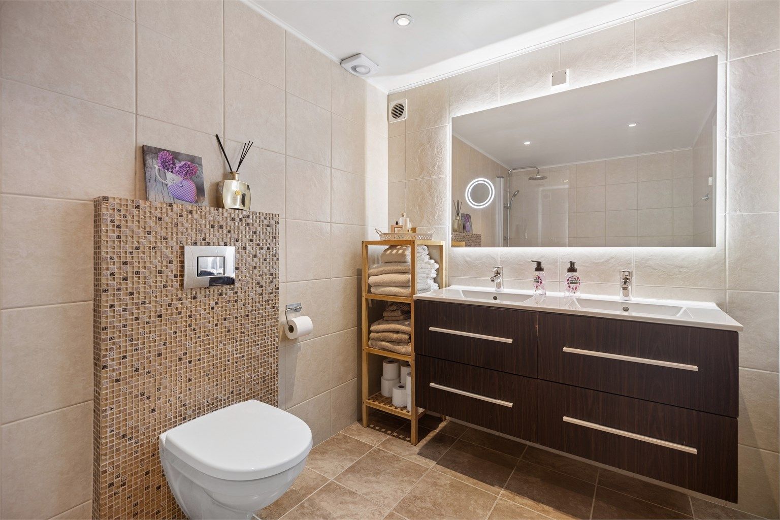 Vegghengt servantinnredning med skuffer og ovenpåliggende dobbel servant, innebygd badekar med hånd- og regndusj samt vegghengt toalett.