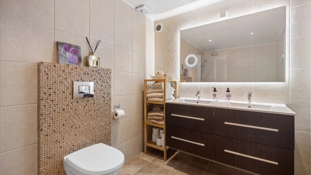 Vegghengt servantinnredning med skuffer og ovenpåliggende dobbel servant, innebygd badekar med hånd- og regndusj samt vegghengt toalett.