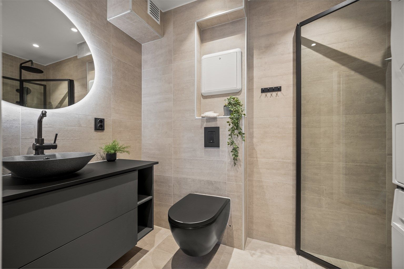 Moderne baderomsinnredning fra 2021 med vegghengt toalett, ovenpåliggende servant og speil med integrert belysning. Foto: Martine Eren Jacobsen