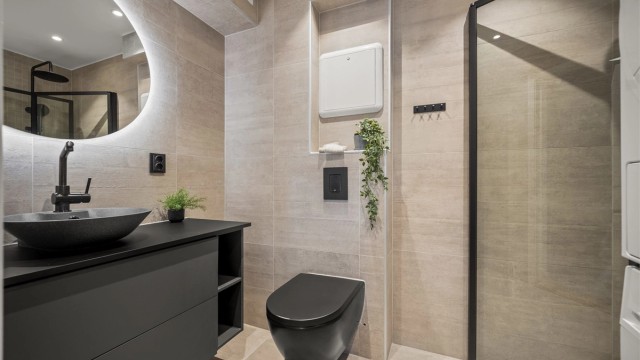 Moderne baderomsinnredning fra 2021 med vegghengt toalett, ovenpåliggende servant og speil med integrert belysning. Foto: Martine Eren Jacobsen