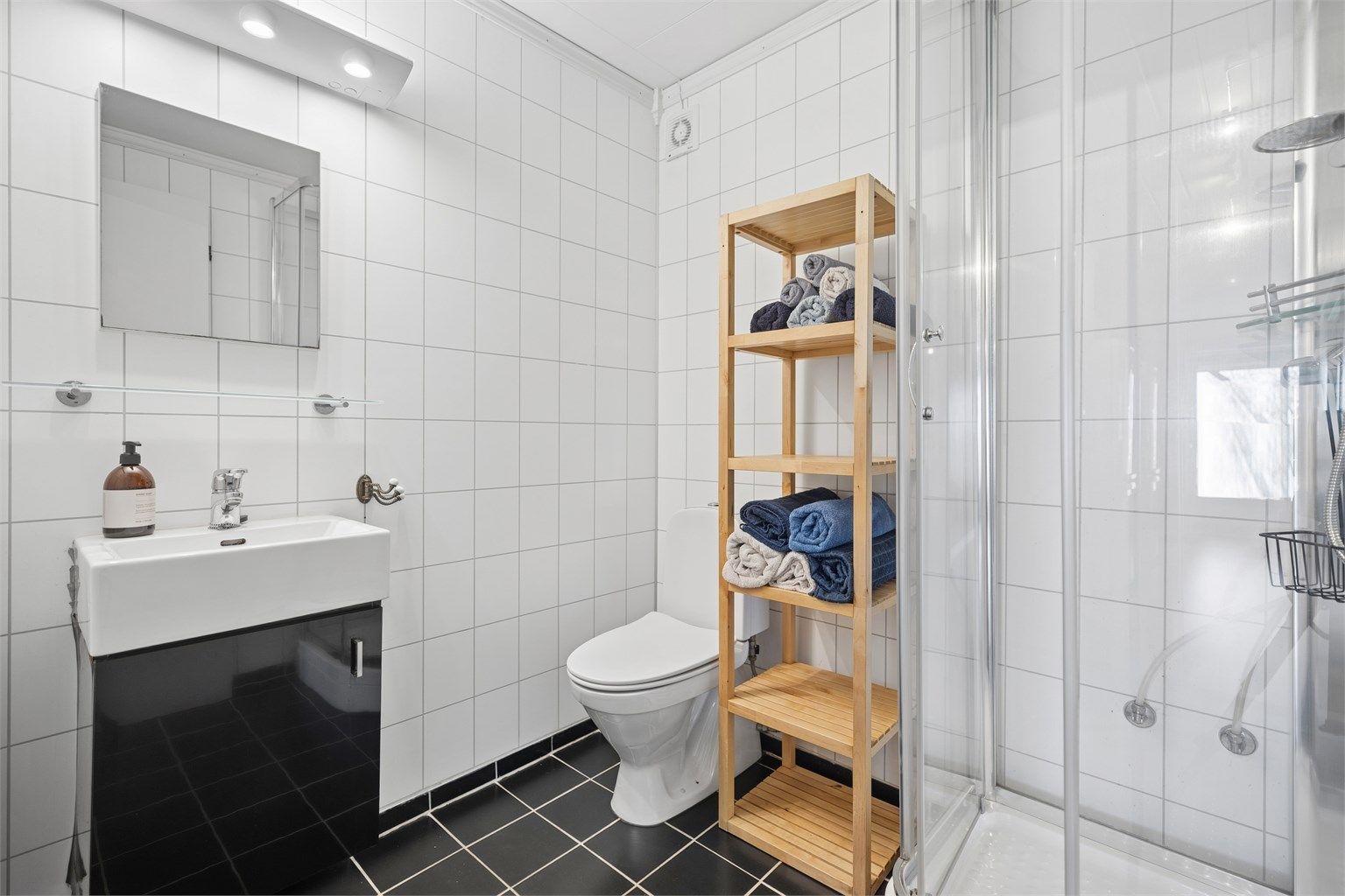 Stilrent, flislagt bad med gulvvarme. Badet er innredet med dusjkabinett, servant i innredning og gulvstående toalett.