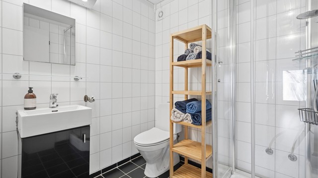 Stilrent, flislagt bad med gulvvarme. Badet er innredet med dusjkabinett, servant i innredning og gulvstående toalett.