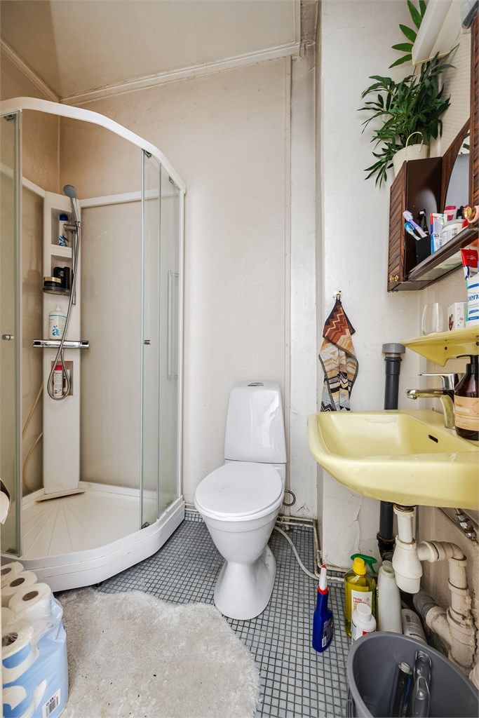 Baderom med fliser på gulv. Badet er innredet med vegghengt servant, speil, dusjkabinett og gulvstående toalett. 