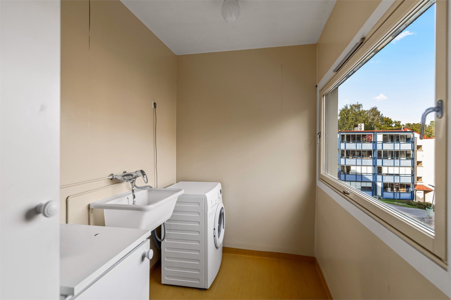 Separat vaskerom med vinylbelegg på gulv, opplegg for vaskemaskin og vegghengt utslagsvask.