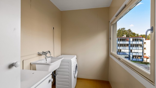 Separat vaskerom med vinylbelegg på gulv, opplegg for vaskemaskin og vegghengt utslagsvask.