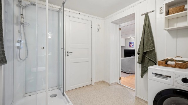 Badet i kjelleretasjen har gulvbelegg med gulvvarme, vegghengt servantinnredning, dusjkabinett, gulvstående toalett og opplegg for vaskemaskin.