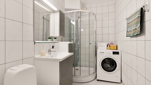 Badet har gulvbelegg og flislagte vegger. Det montert innredning med slette fronter, heldekkende servant. Badet er også utstyrt med overskap, speil, overlys og stikkontakt. Dusjkabinett og gulvstående toalett. Opplegg for vaskemaskin.