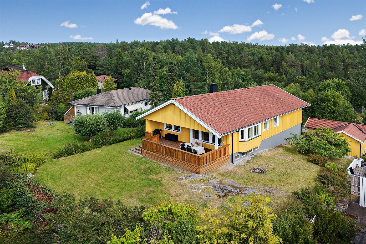 Tomten er pent opparbeidet med gressplen og beplantning, omkranset av grønne omgivelser.