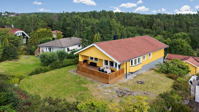 Tomten er pent opparbeidet med gressplen og beplantning, omkranset av grønne omgivelser.