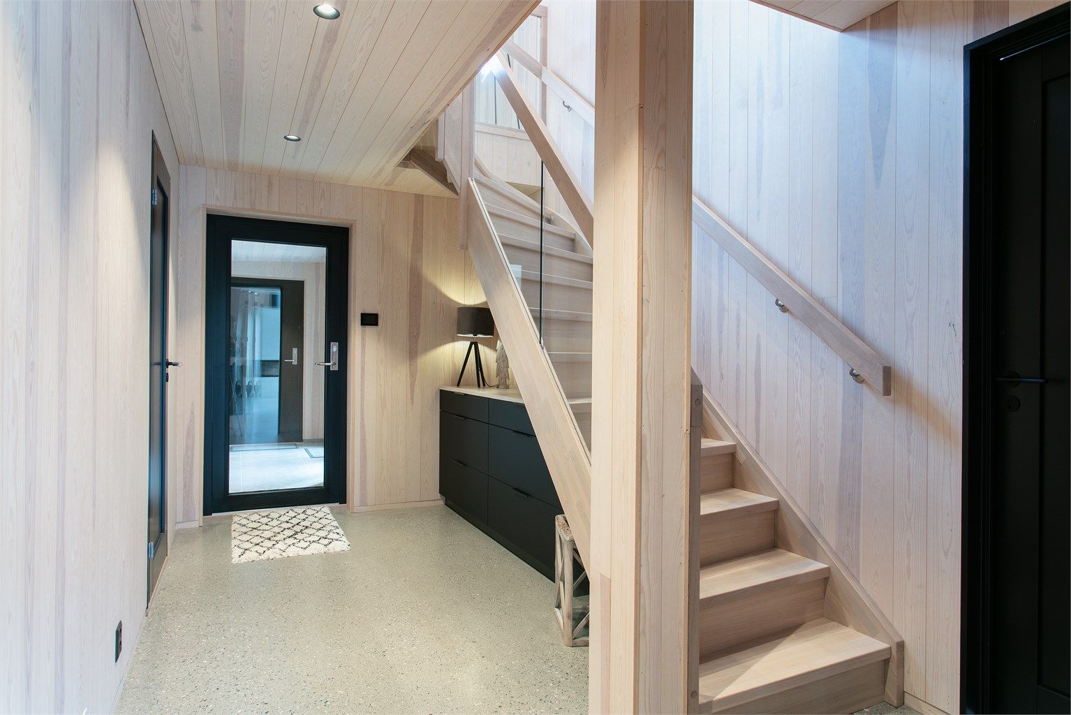 Hall med innvendig tretrapp og glassrekkverk opp til loftsetasjen.