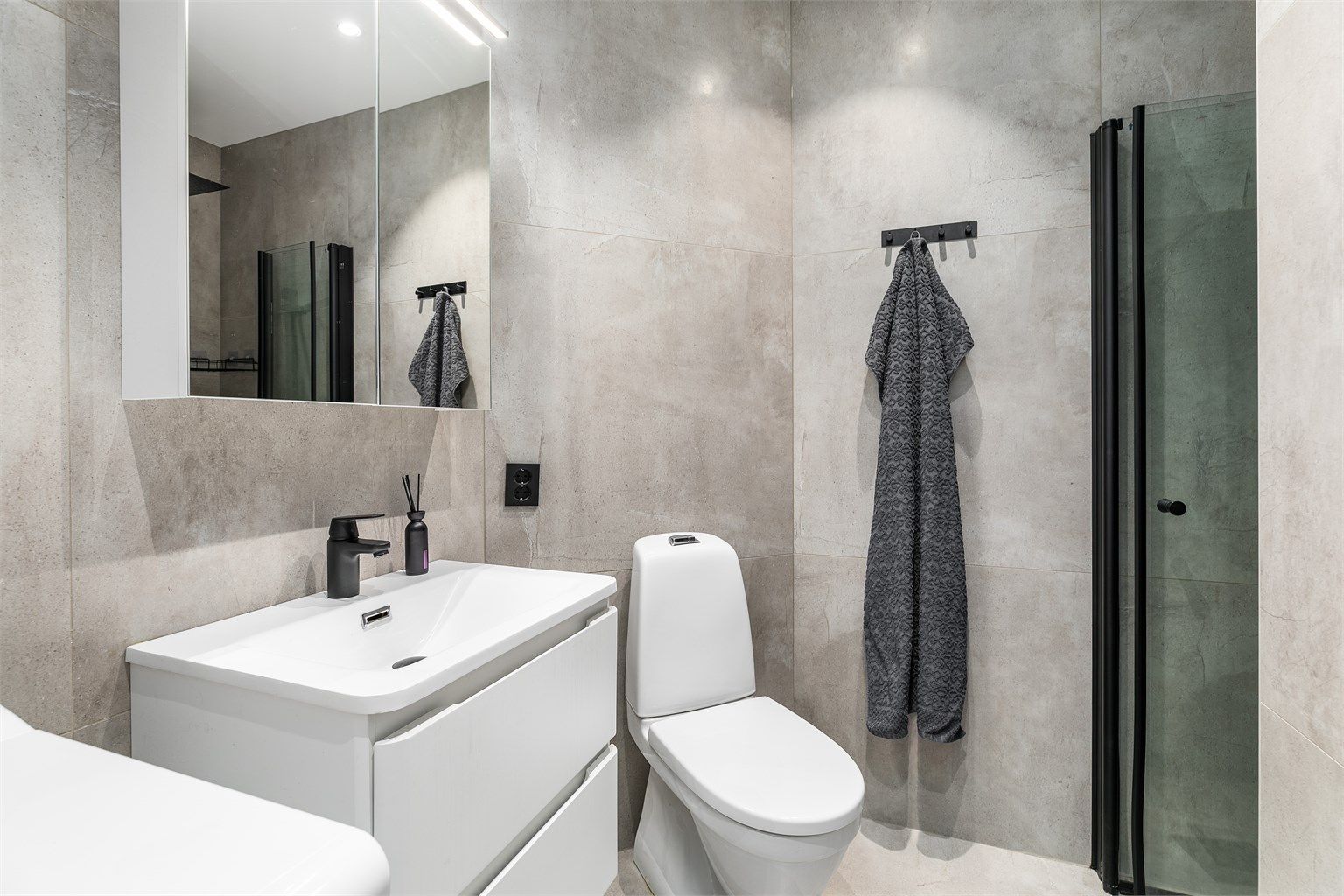 Etter ombygging og oppgradering i 2022 er badet stilfullt og moderne. Like fliser på gulv og vegger skaper helhet, sorte elementer danner kontrast.