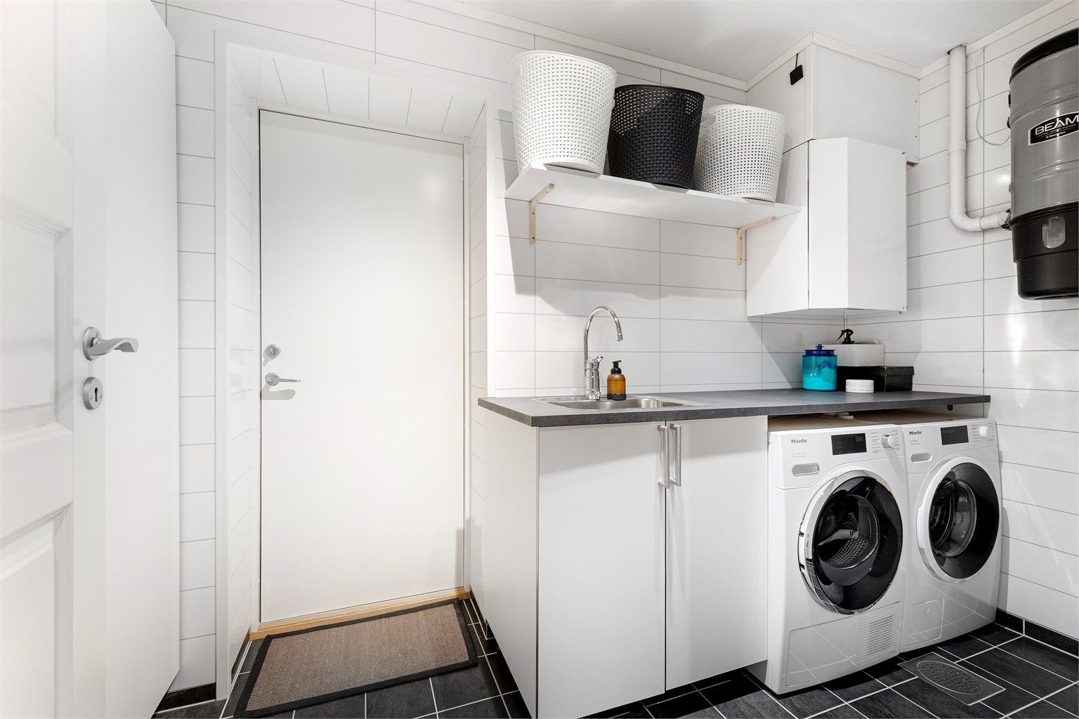 Praktisk vaskerom med flislagt gulv, varmekabler og direkte utgang til garasjen.