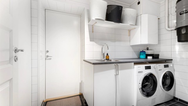 Praktisk vaskerom med flislagt gulv, varmekabler og direkte utgang til garasjen.