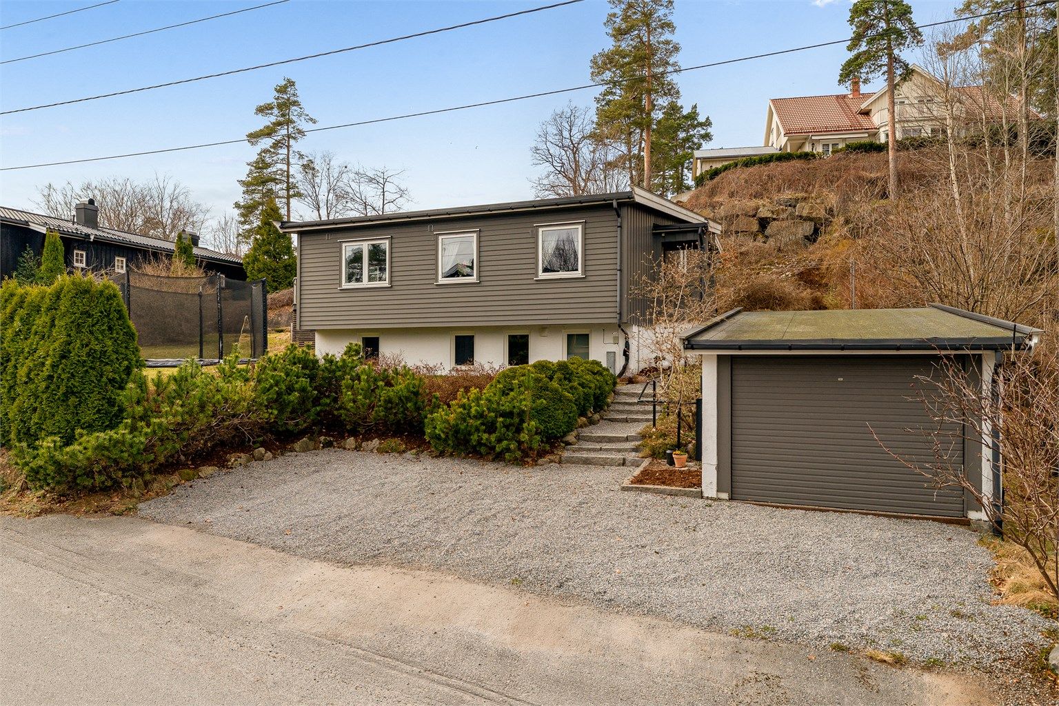 Eiendommen har en frittstående garasje med elbillader og en pent opparbeidet, gruset gårdsplass.