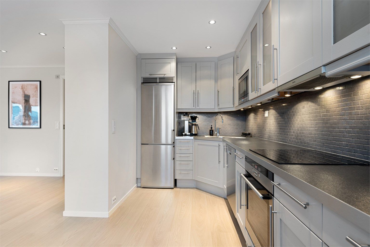 Integrert stekeovn og platetopp fra 2025. Frittstående oppvaskmaskin og kjøleskap med fryser. Ventilator i overskap. Det er lagt fliser mellom kjøkkenbenk og overskap. 